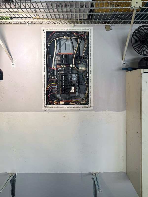 The same garage wall with a new panel set in the wall, breakers installed and wiring visible before the cover goes on